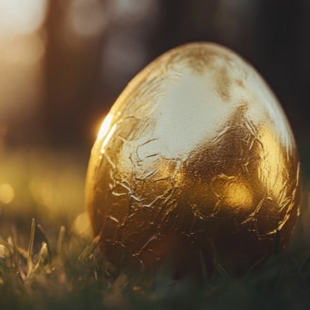 A large egg wrapped in golden foil sat on the grass with the sun reflecting against it